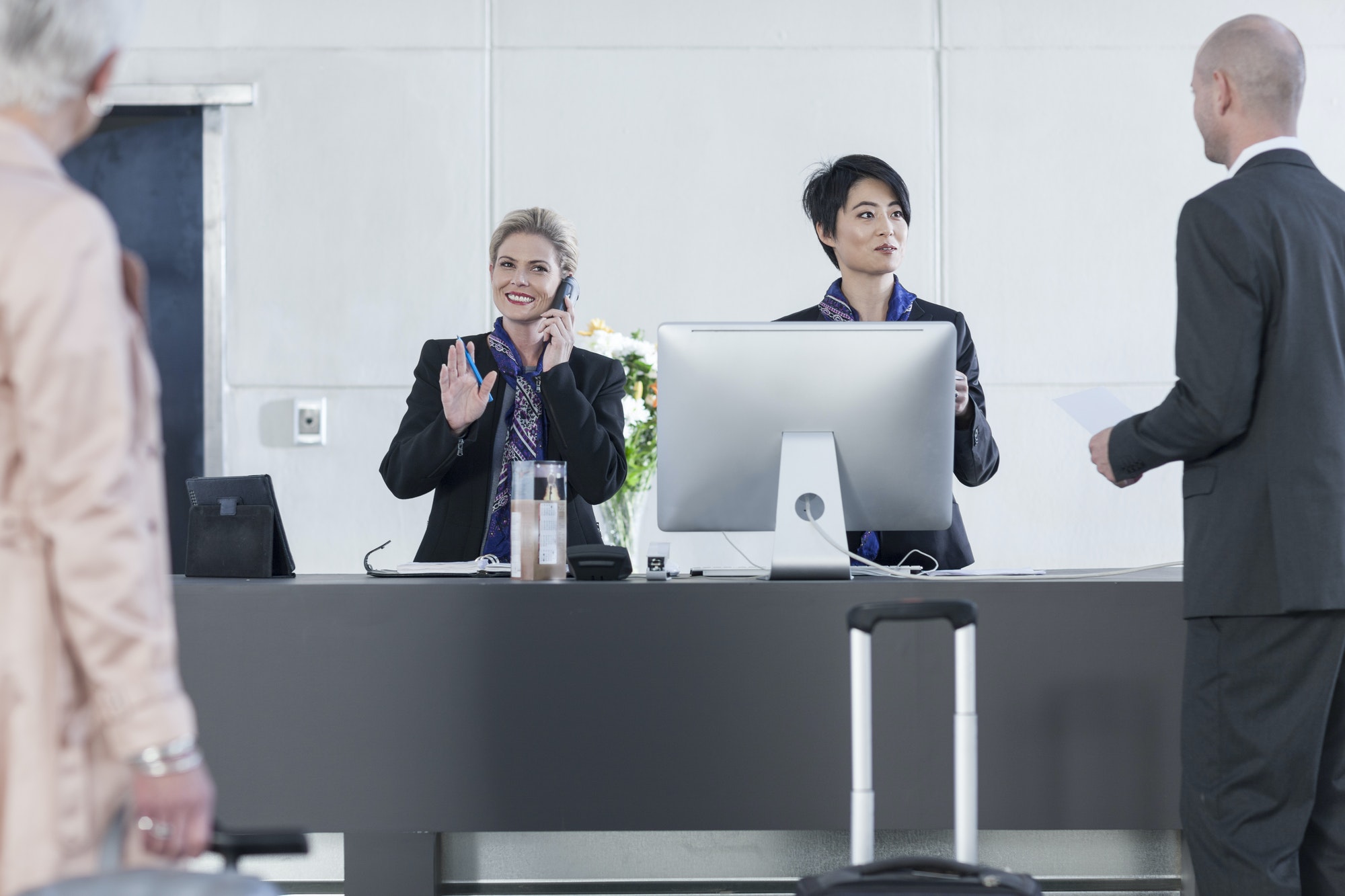 Two women behind reception desk in hotel lobby helping guests