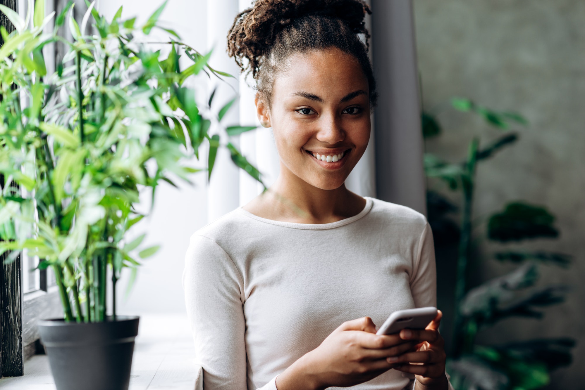 Beautiful african american girl in casual clothes uses smartphone and smiles