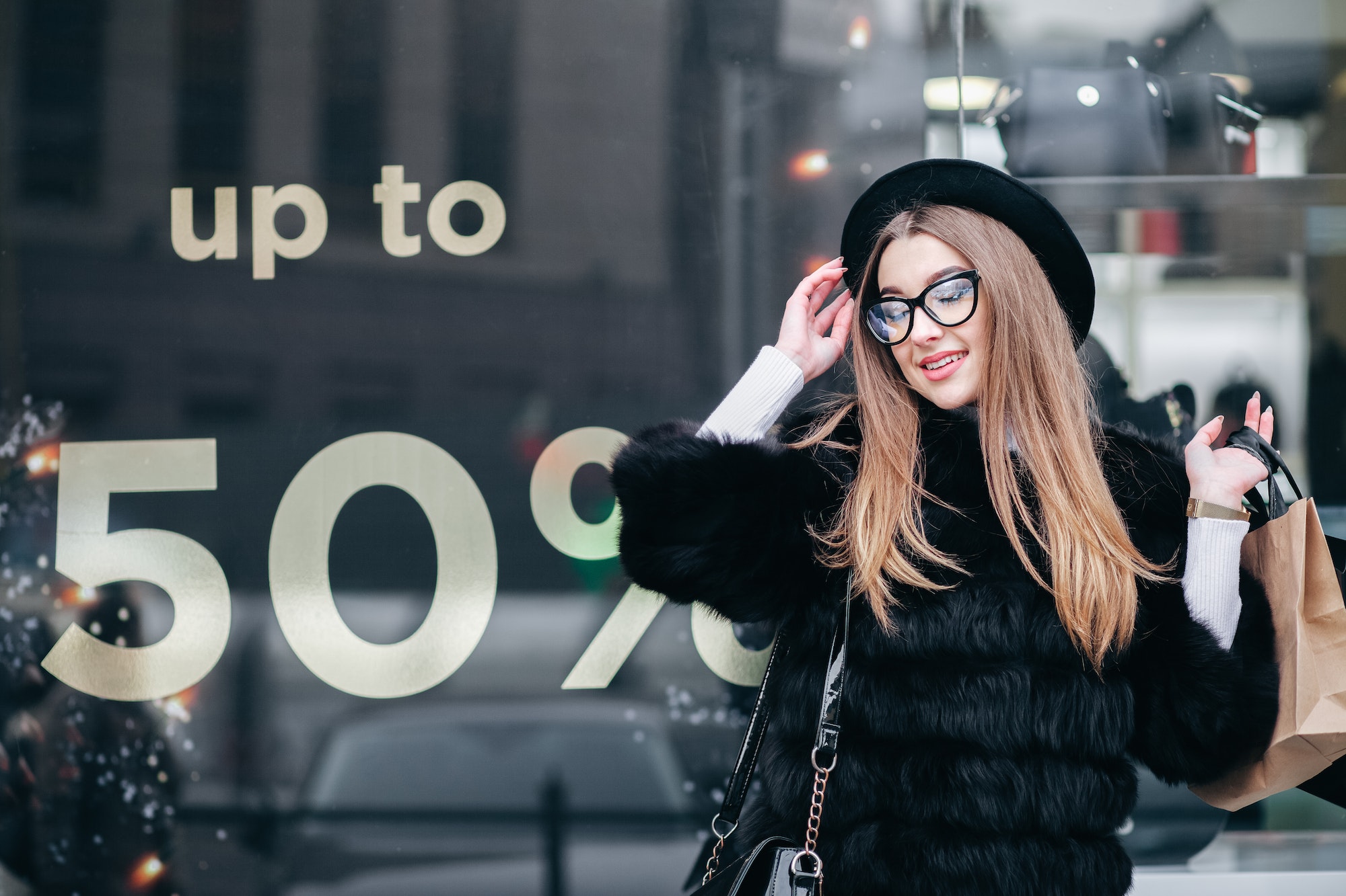 Elegant woman with shopping bags is standing near a shop window with clothes.