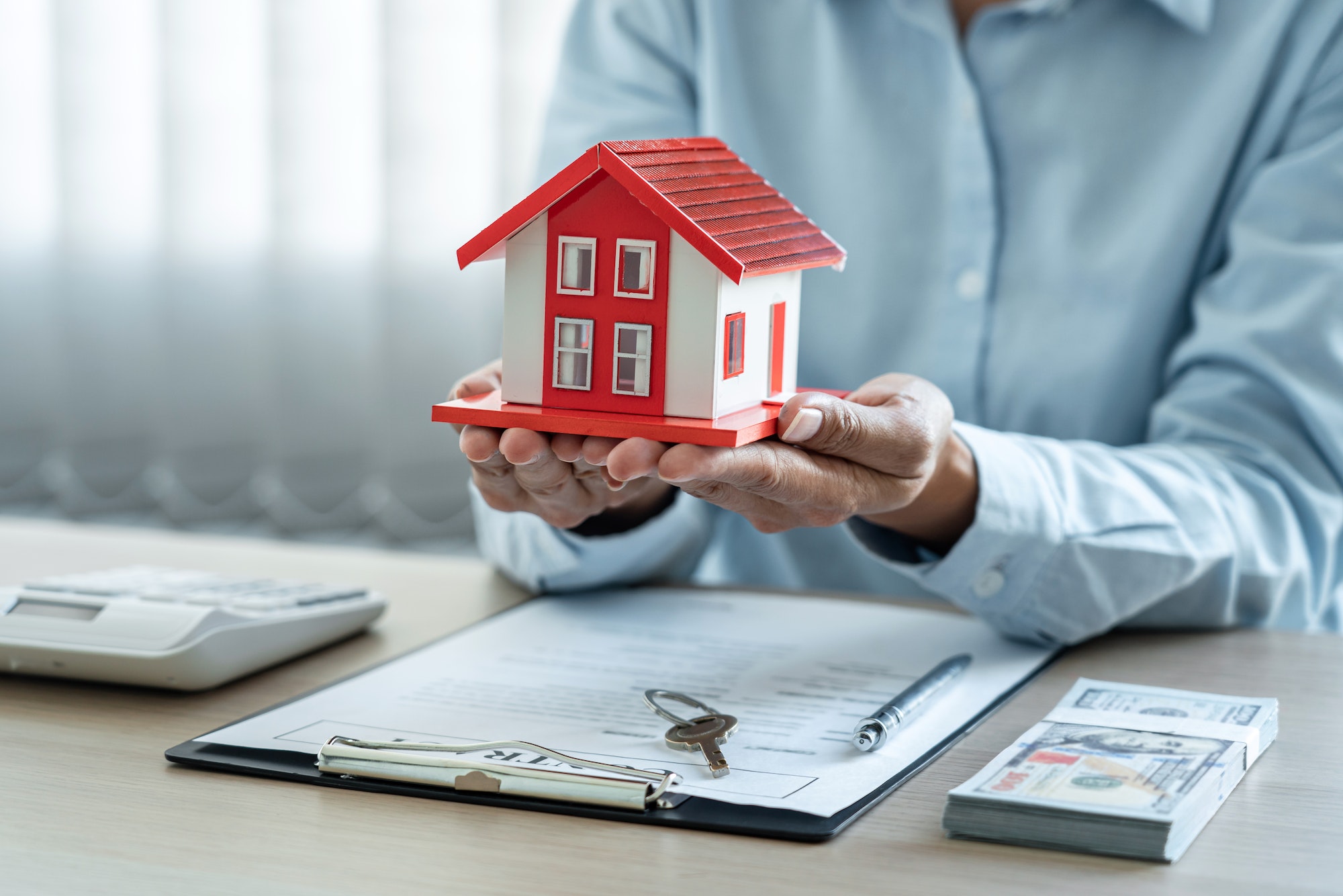 Female real estate agent is use hands holding house of red roof for the concept of real estate