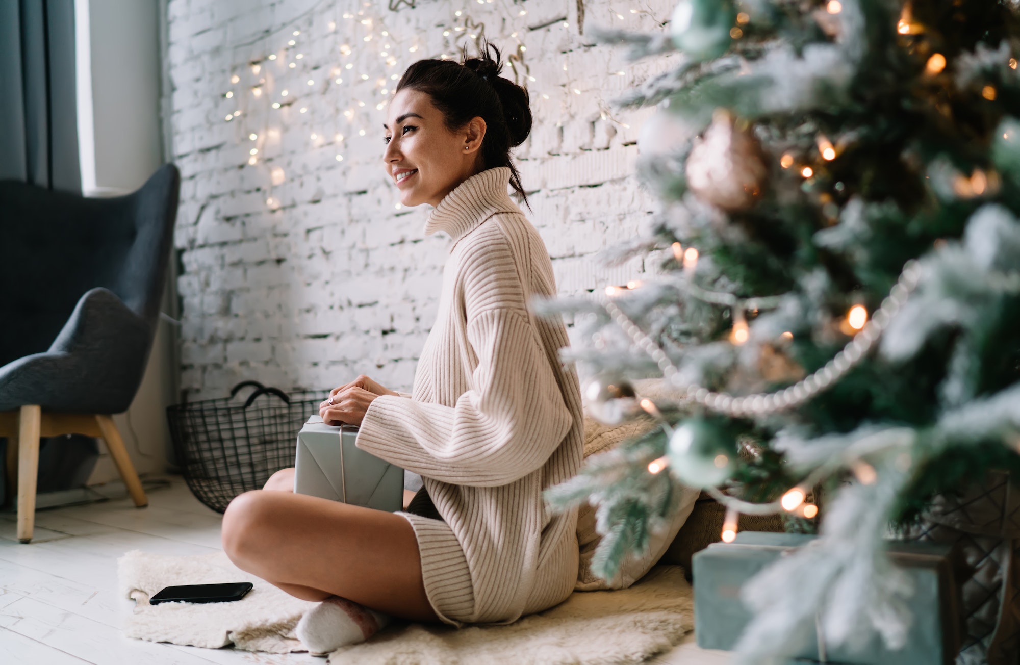 Woman opening gift near Christmas tree at home